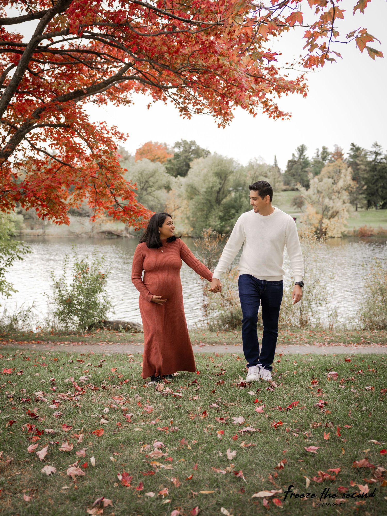 Maternity photography session by a lake with red autumn leaves and natural scenery.