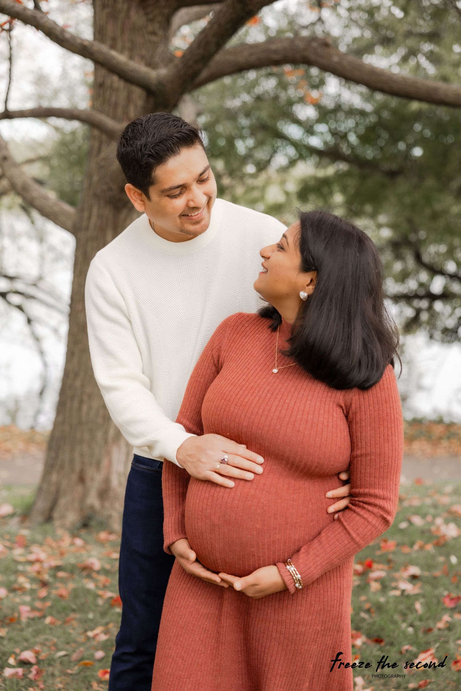 Intimate maternity photos captured under autumn trees with couple in rust and white attire.