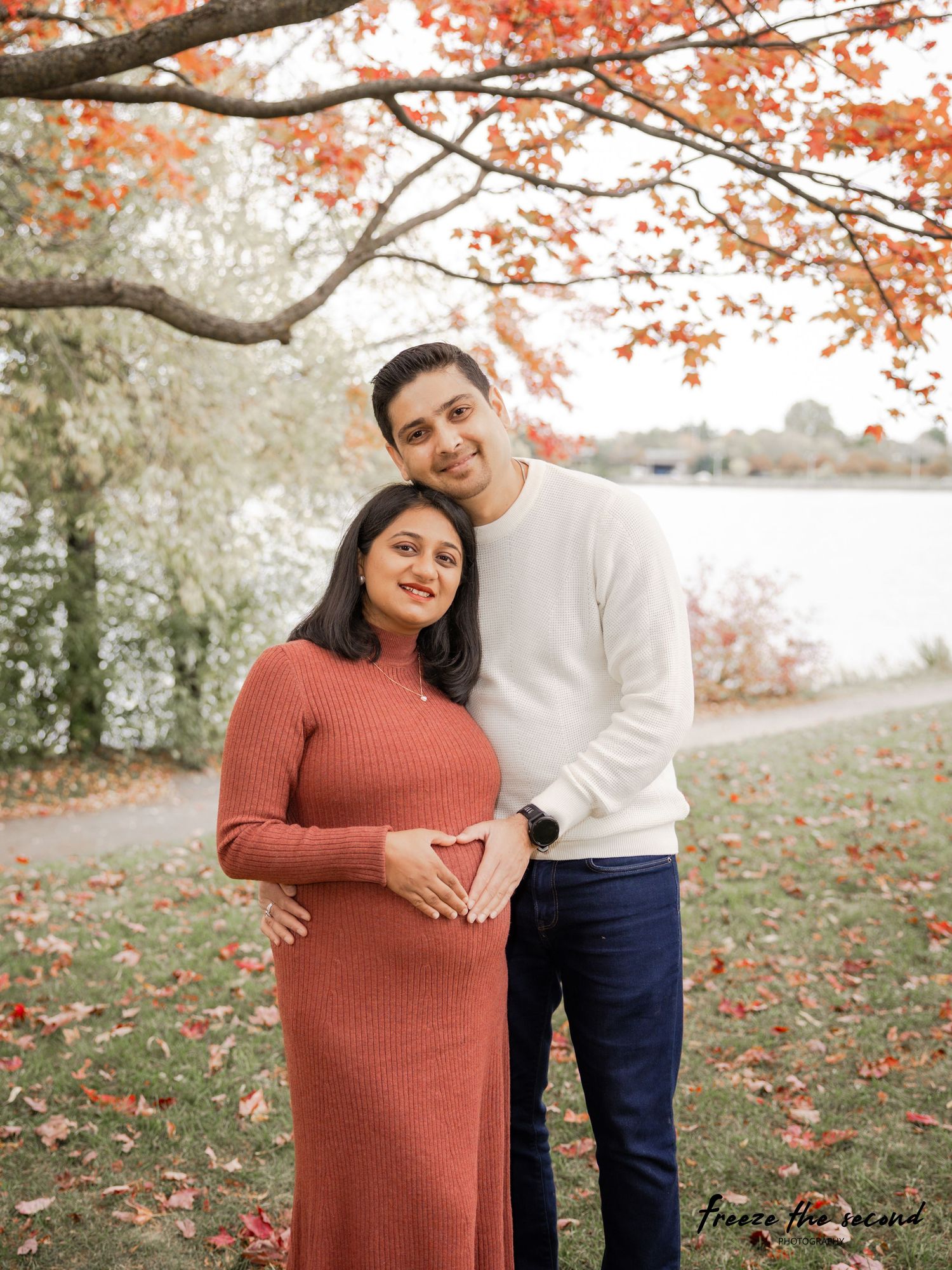 Maternity photoshoot under red autumn maple trees with couple in coordinating rust and white outfits.