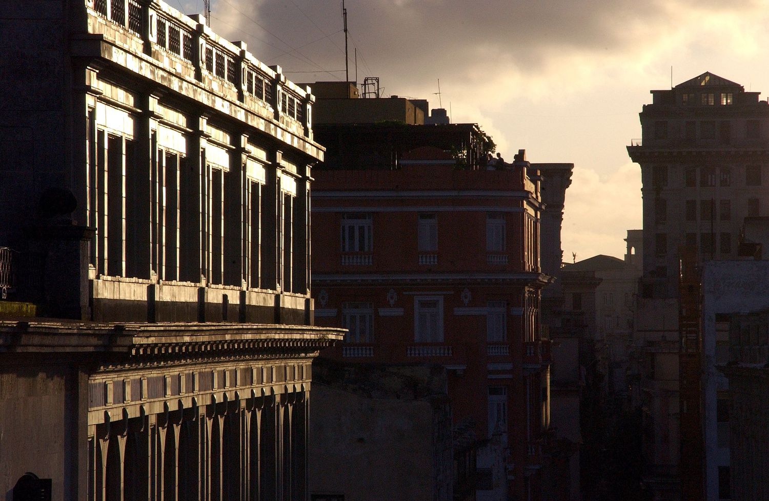 Row of buildings silhouetted against dramatic sunset sky with dark shadows.