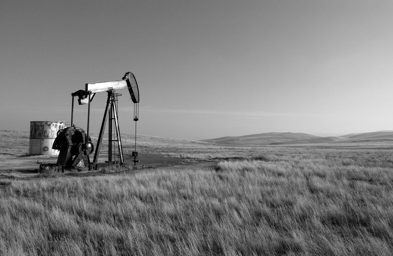 Black and white panoramic view of oil pumps and grasslands stretching across a vast prairie landscape.
