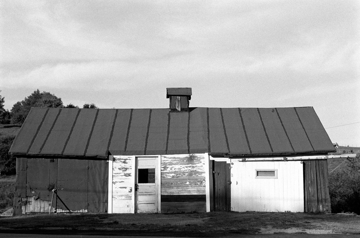 Row of low industrial or commercial buildings with metal roofs in black and white.