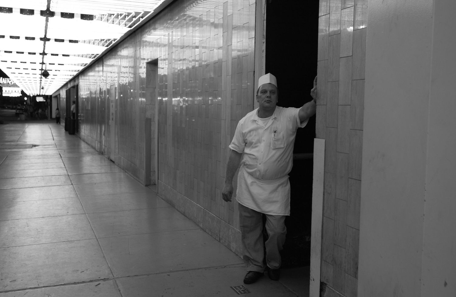 Person standing in long empty corridor with glass walls.
