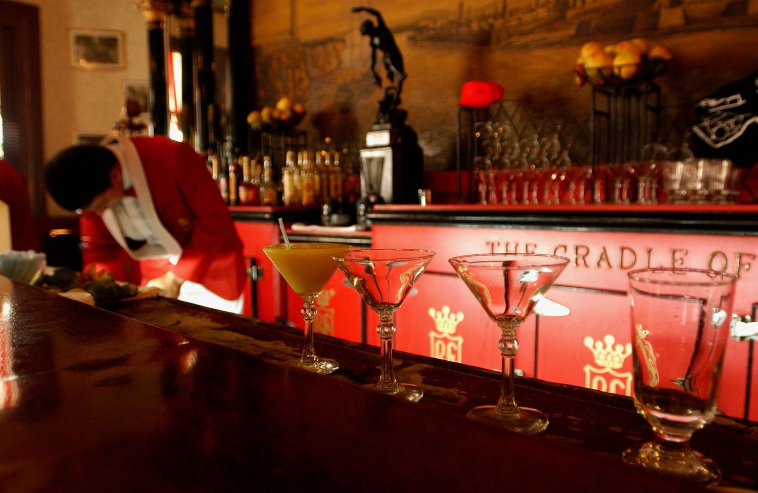 Red-lit modern bar interior with bottles and glassware displayed on illuminated shelves.