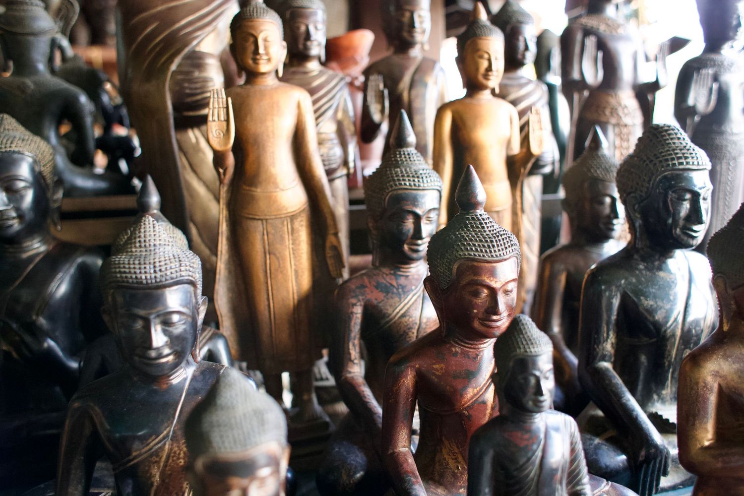 Collection of ancient Buddha statues crowded together in various sizes and styles.
