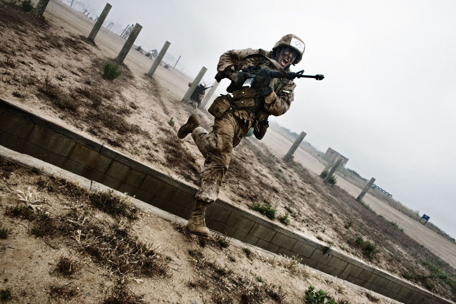 Combat units practicing tactical maneuvers along a desert wall barrier.