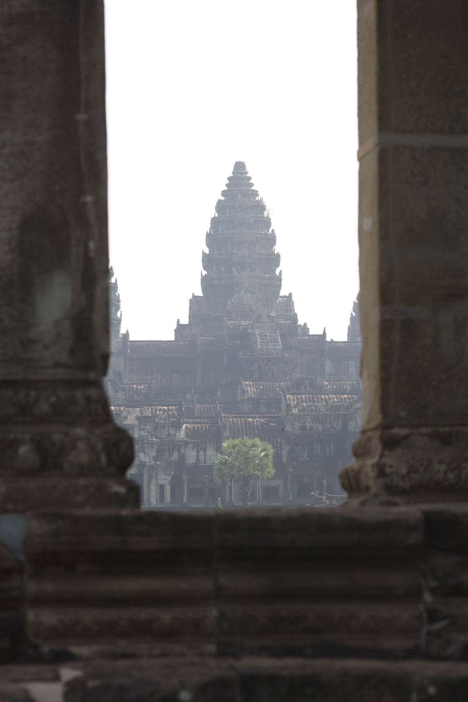 Silhouetted view of Angkor Wat temples through stone pillars at dawn.