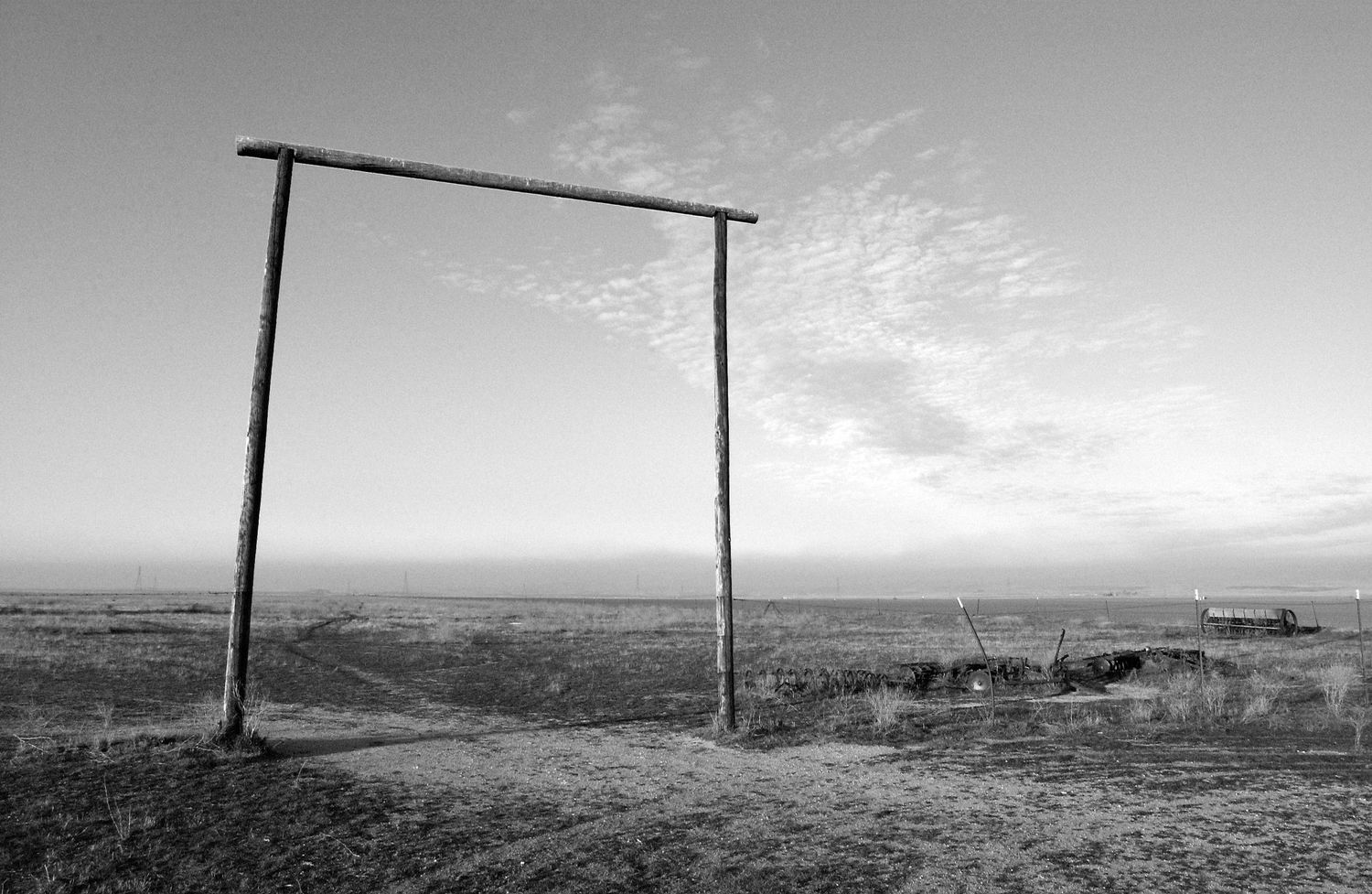 Panoramic black and white landscape with wooden poles stretching across rolling hills under dramatic clouds.