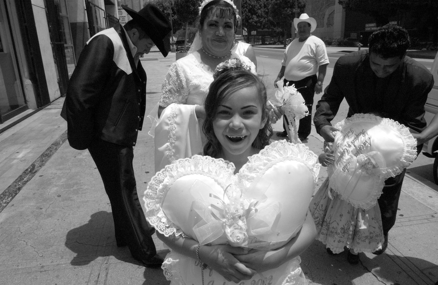 Girl in white dress holding large decorative satin pillows outdoors.