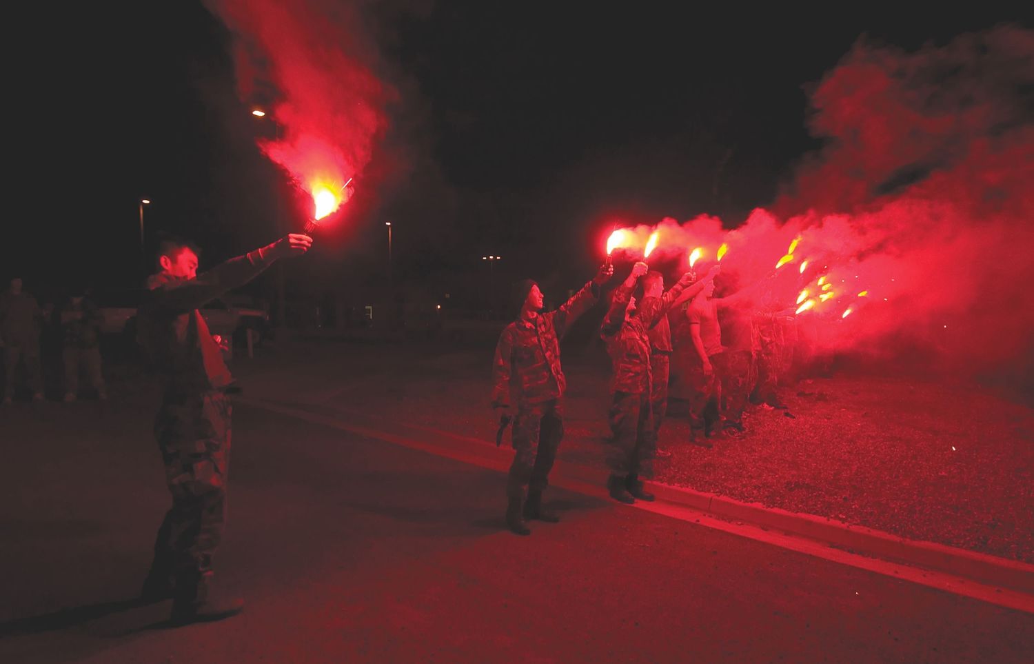 Night training exercise with red flares illuminating dark terrain.
