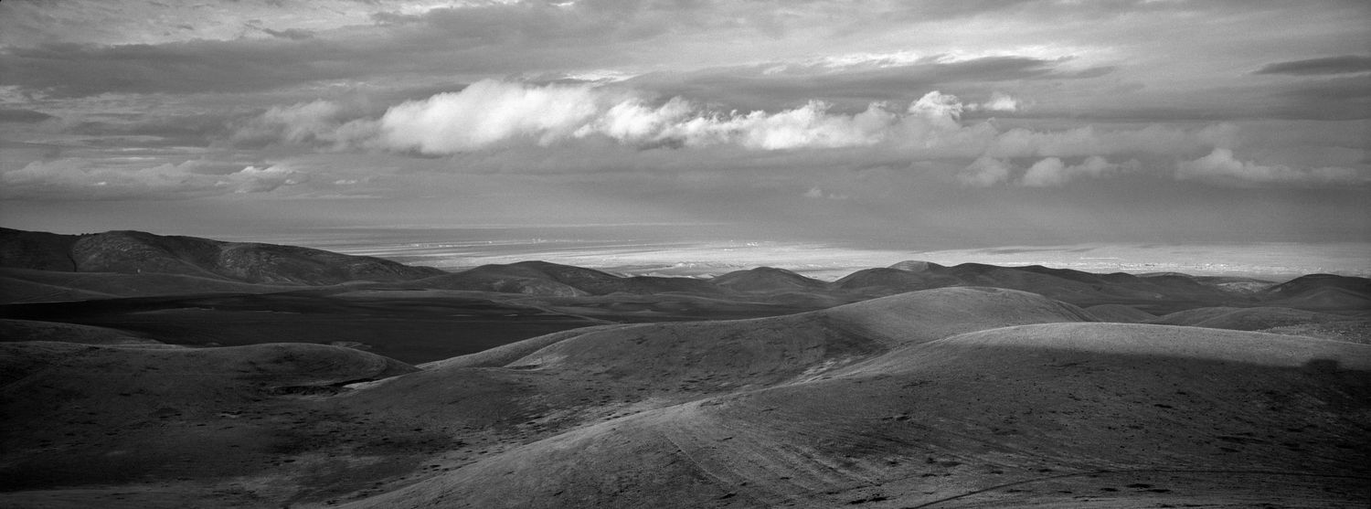 Series of stark desert hills and valleys captured in monochromatic tones against a cloudy sky.