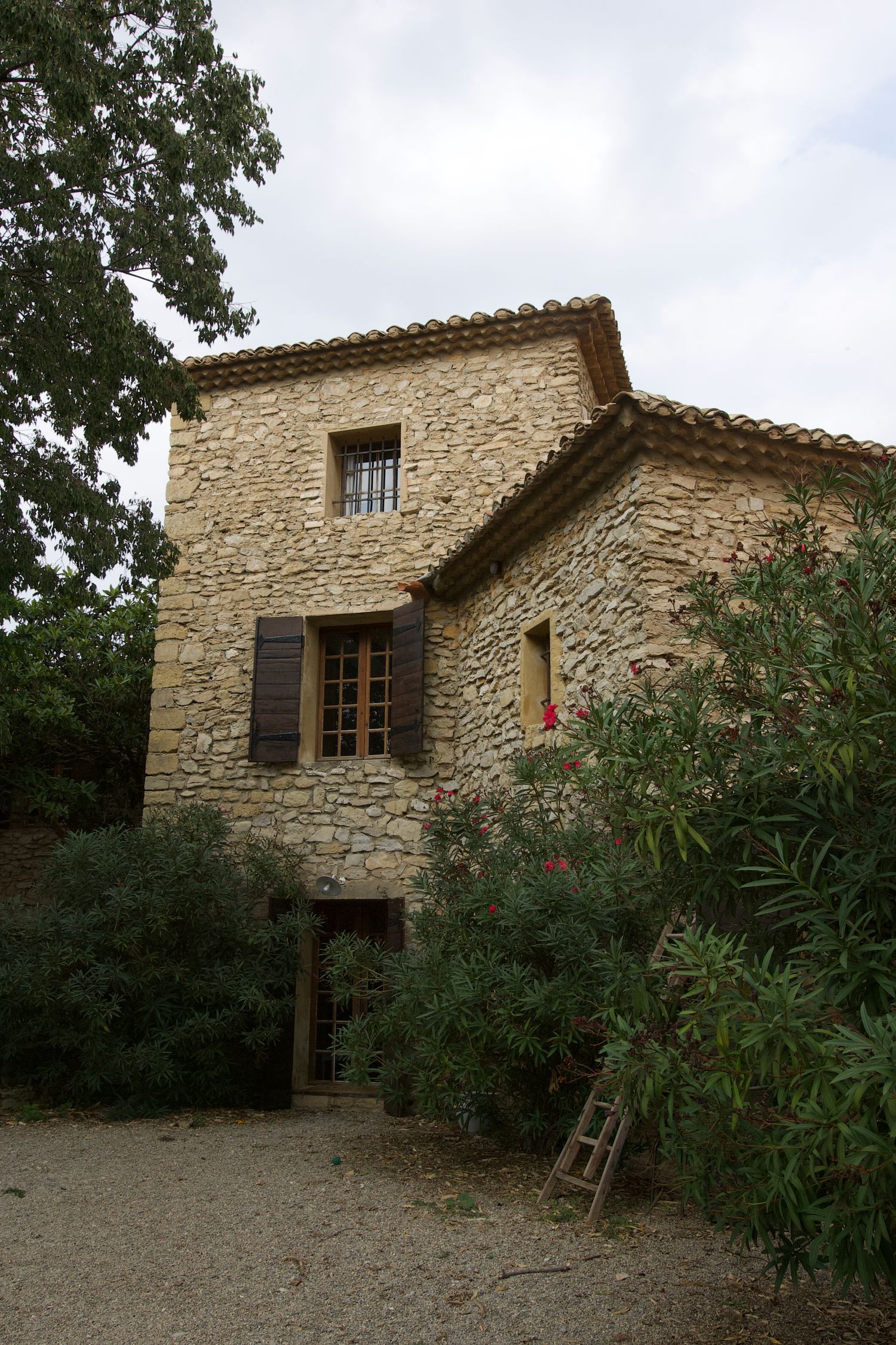 Rustic stone cottage with wooden shutters and terra cotta roof tiles in Provence countryside.