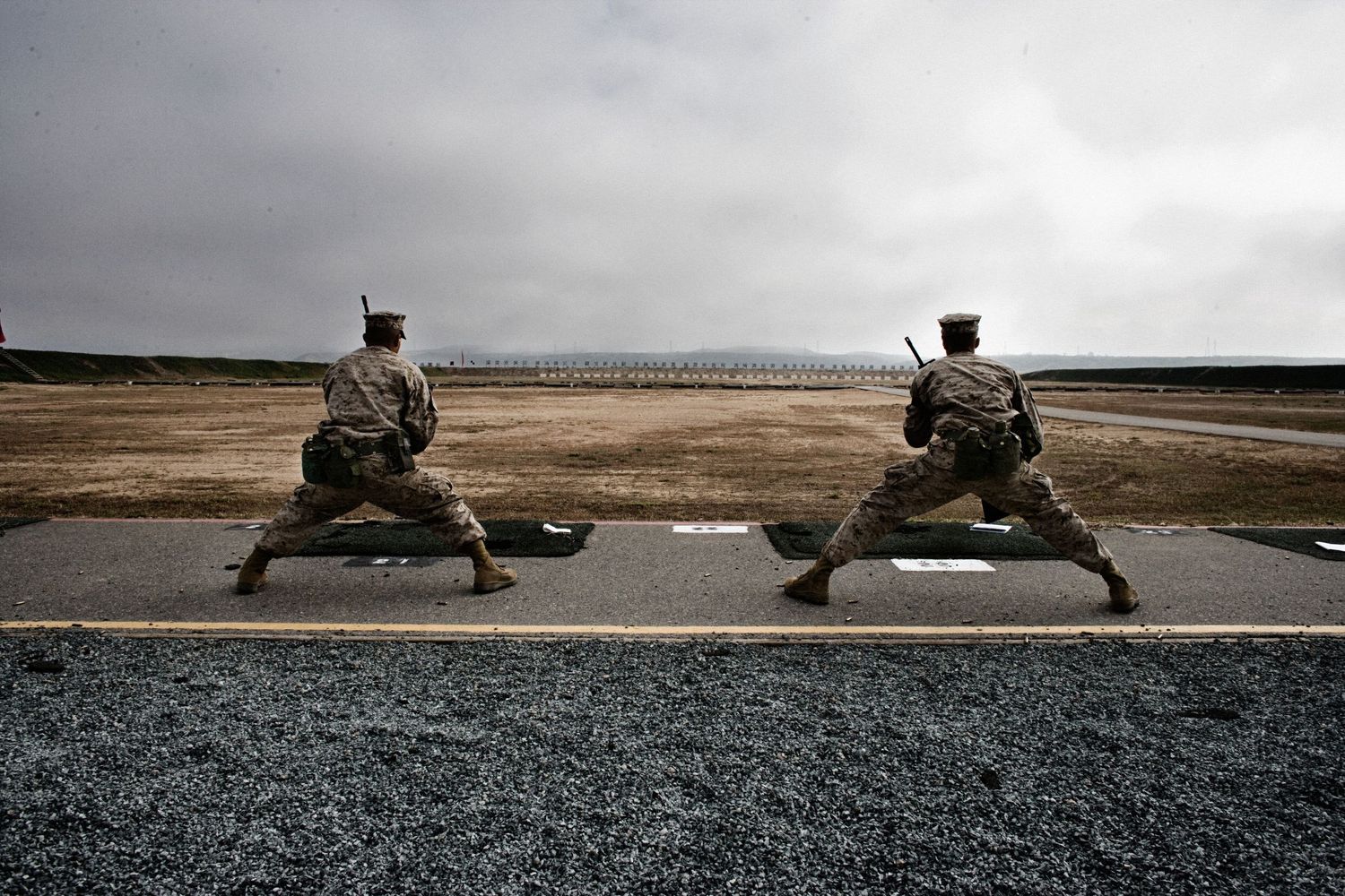 Military snipers lying prone in position with rifles on a field during training.