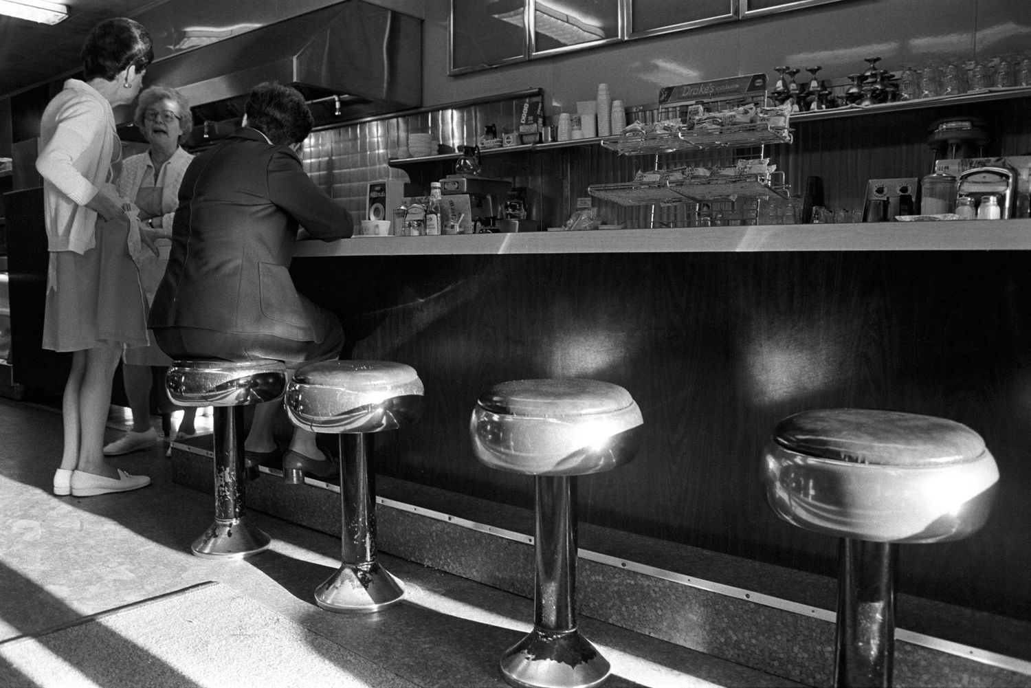Vintage black and white photo of classic American diner counter with chrome stools.