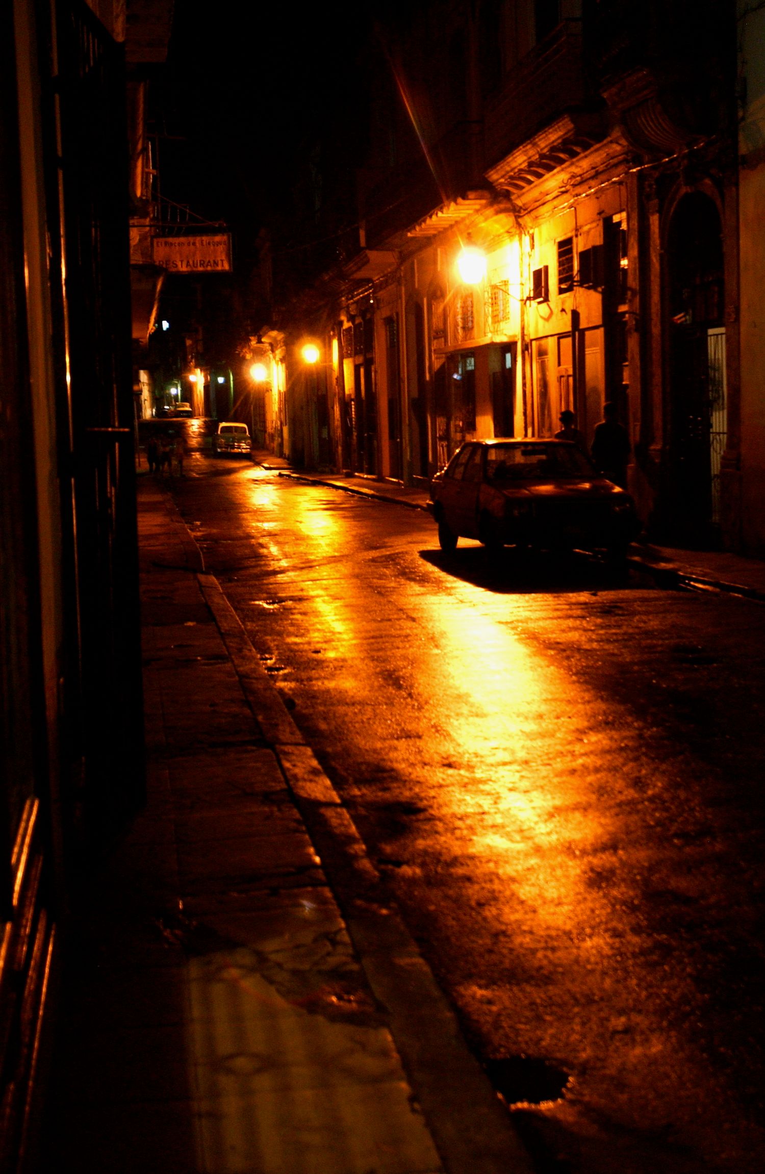Nighttime urban street illuminated by warm glowing streetlights reflecting off wet pavement.
