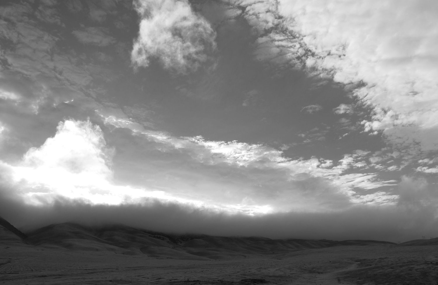 Wide panoramic view of dramatic cloud formations over a mountain landscape in black and white.
