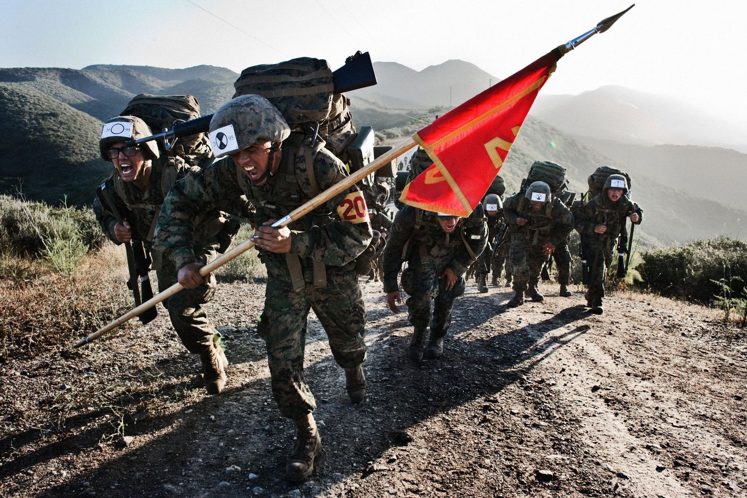 Soldiers marching in formation carrying red flags during military training.