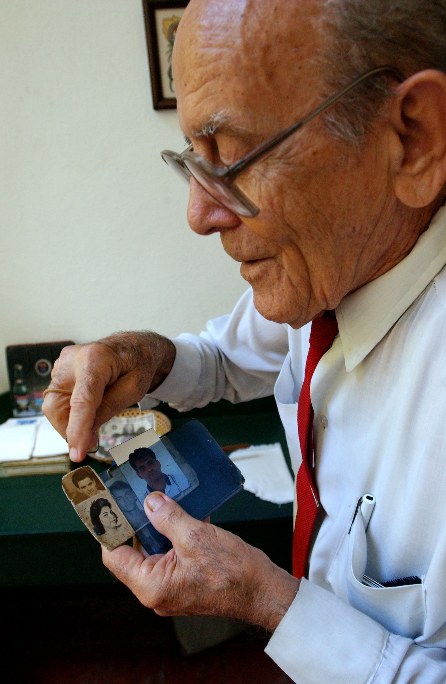 Person examining a small object while wearing glasses and a white shirt with red tie.