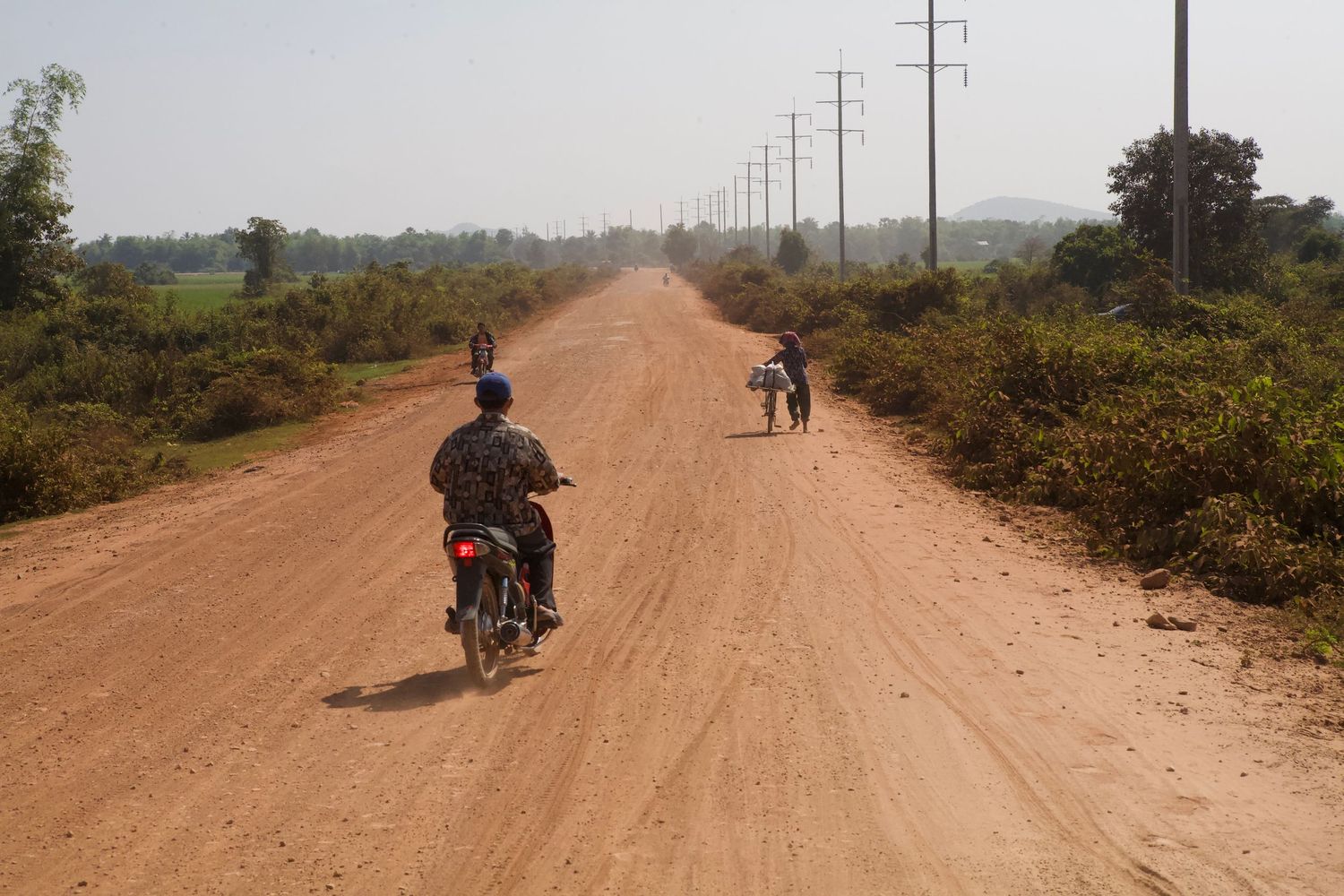 Dusty rural road with travelers on motorcycles in Southeast Asia.