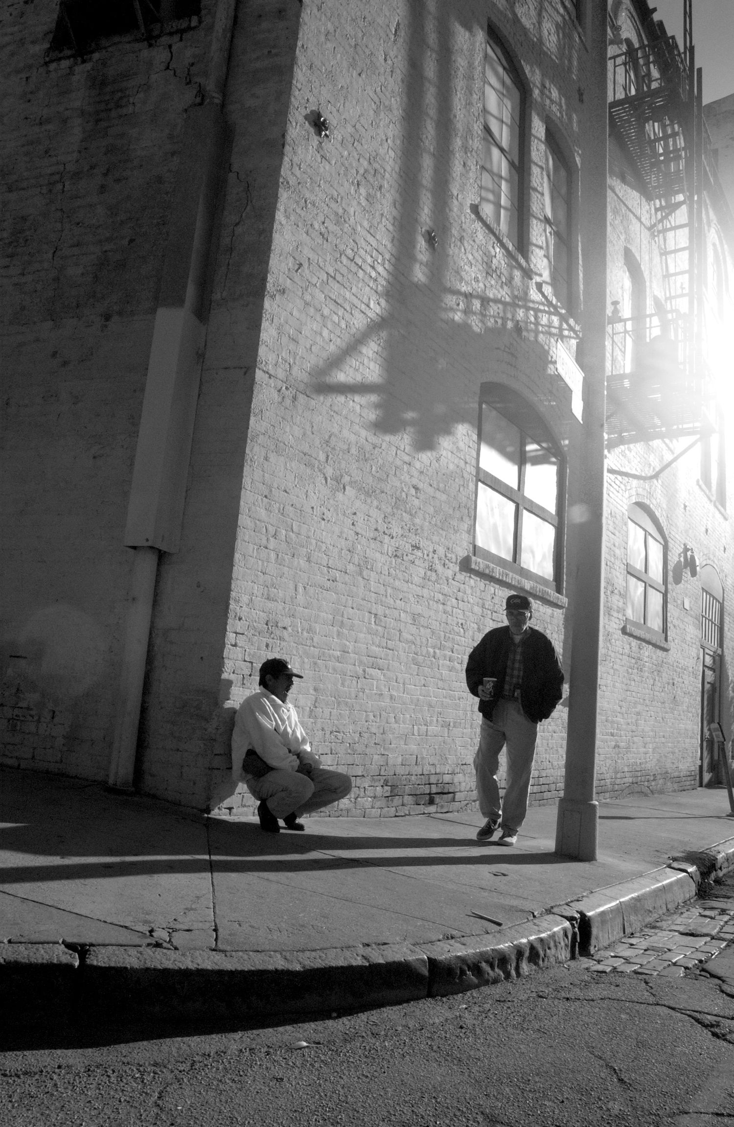 Sunlit urban alleyway with white brick walls casting dramatic shadows.