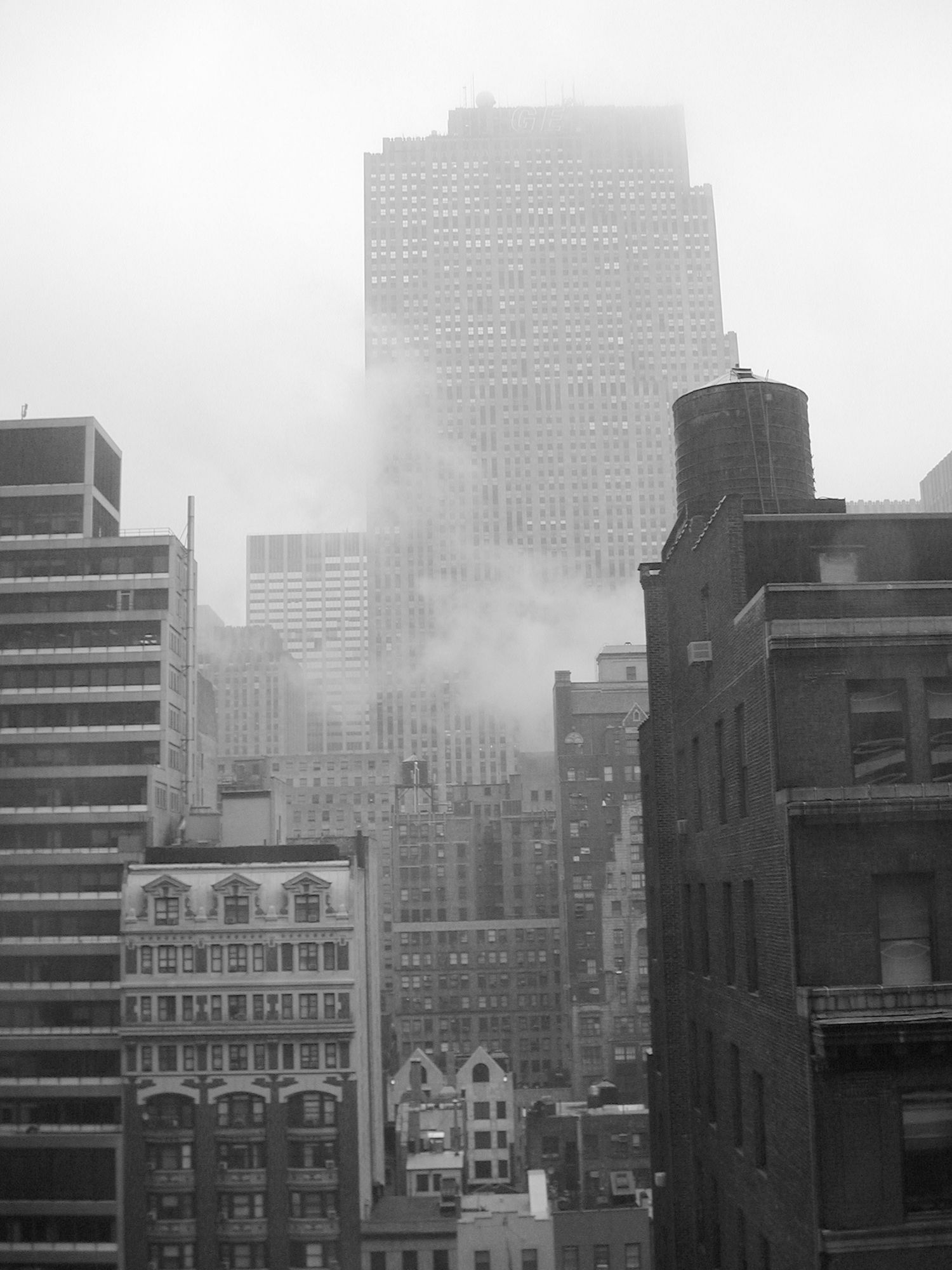Foggy cityscape of tall buildings and skyscrapers in a monochromatic urban setting.
