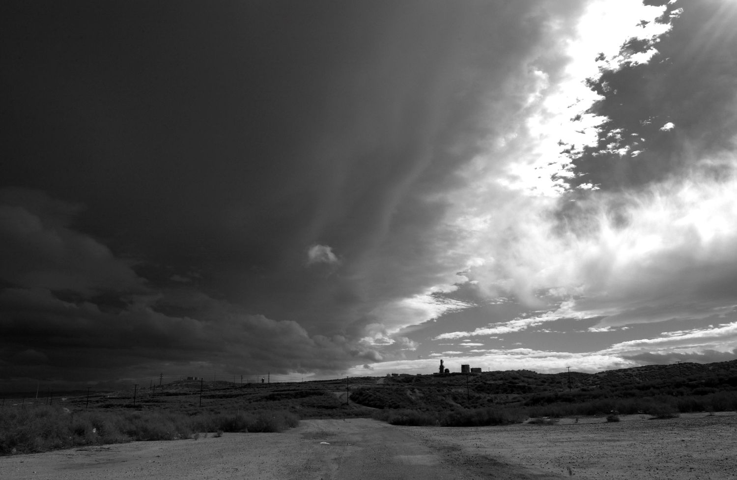 Dramatic black and white skyscape with storm clouds and sunbeams stretching across mountain terrain.