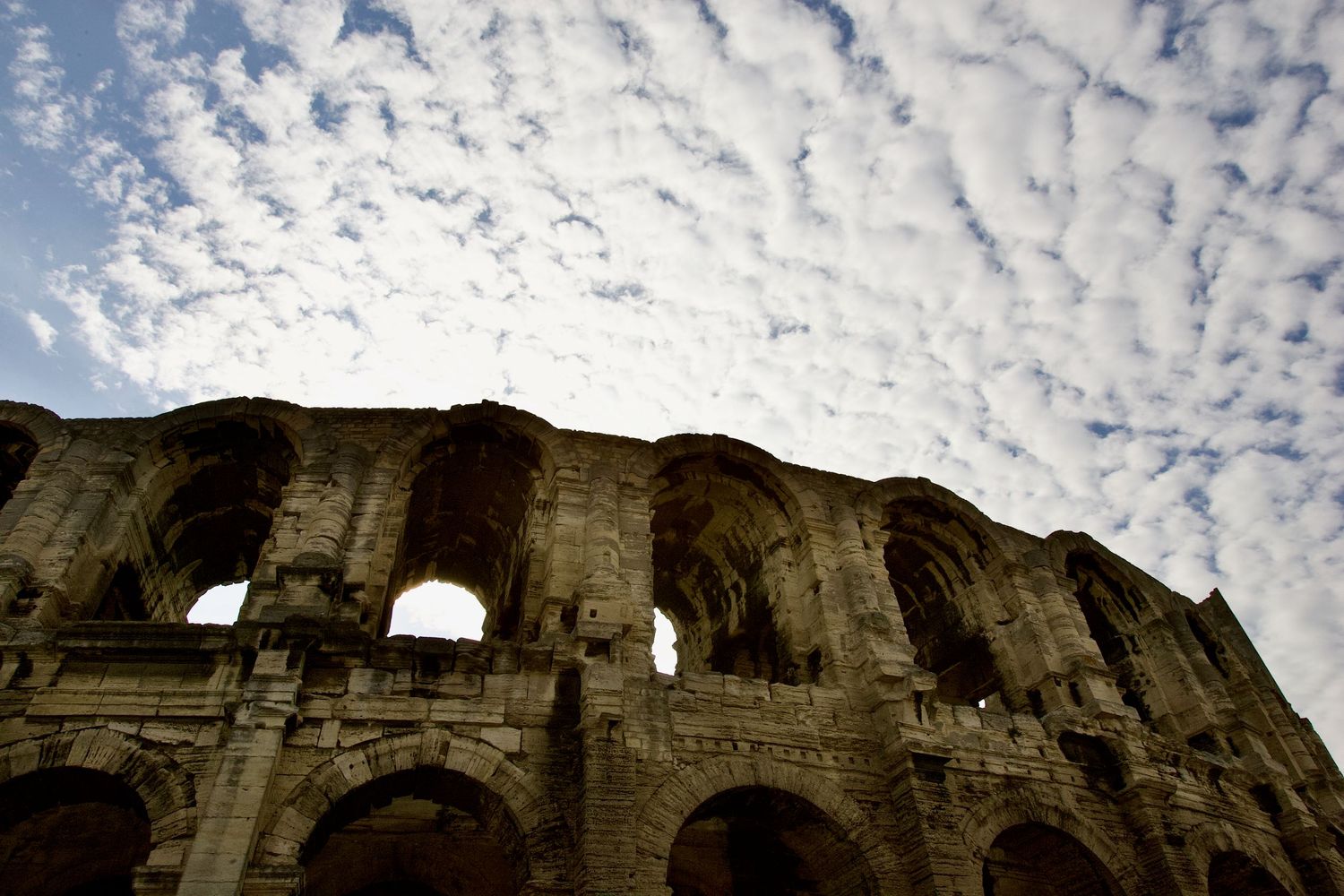 Gothic stone archways and walls photographed from below against dramatic cloudy sky.