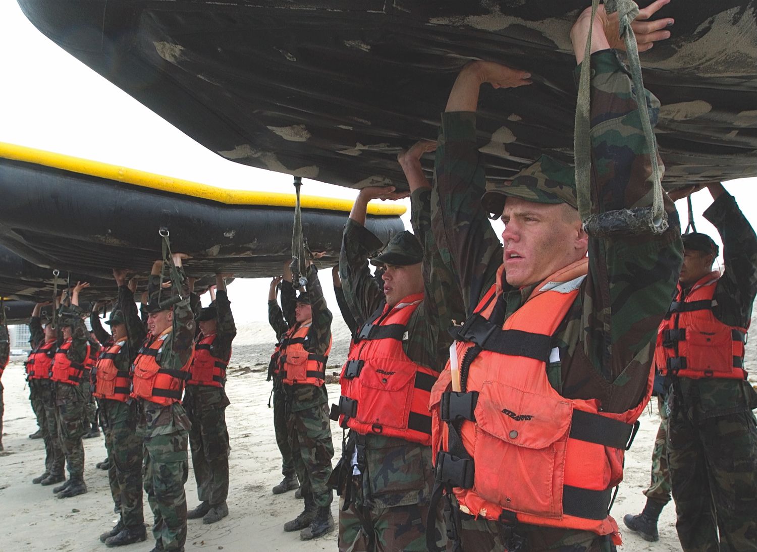 Military personnel in orange life vests lined up during training exercise.