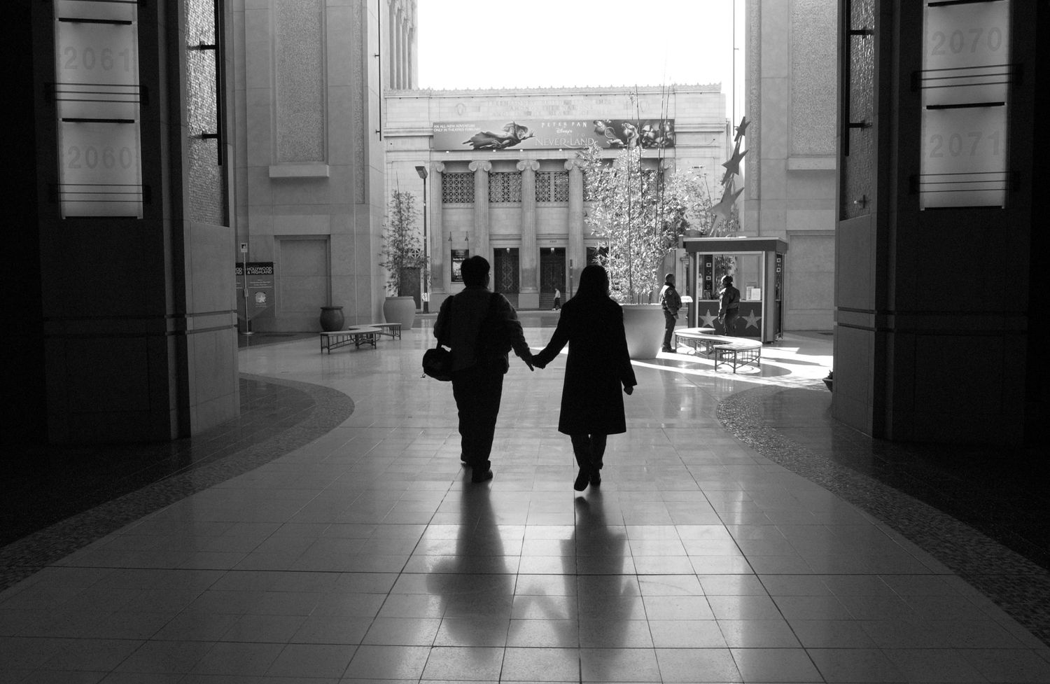 Black and white interior hallway with silhouettes of people walking.
