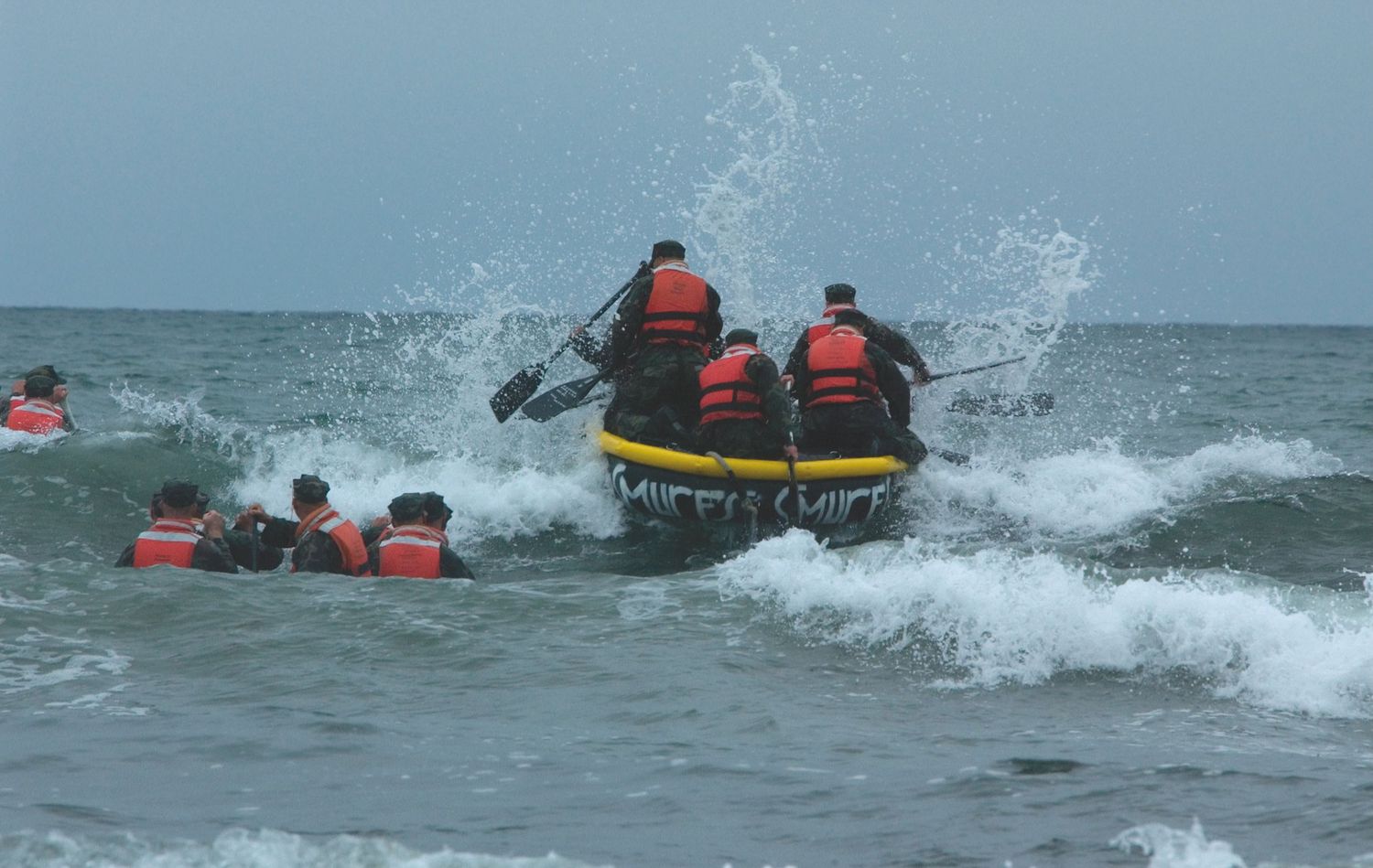 Military personnel conducting water rescue training exercises in rough ocean waves.