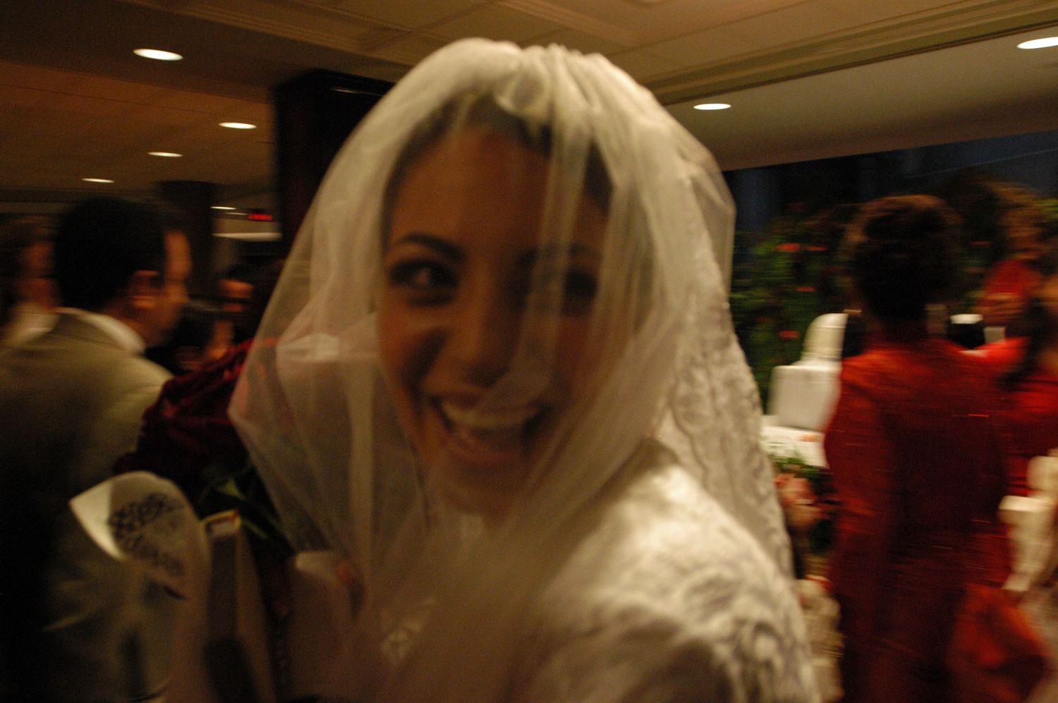 Blurry candid photo of bride wearing white veil at indoor celebration.