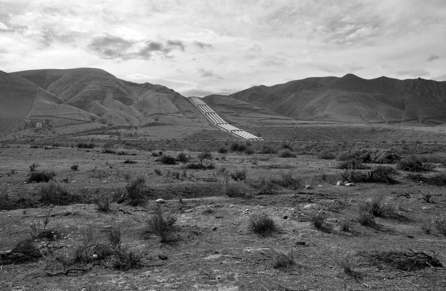 Panoramic black and white landscape of barren hills and mountains under cloudy skies.