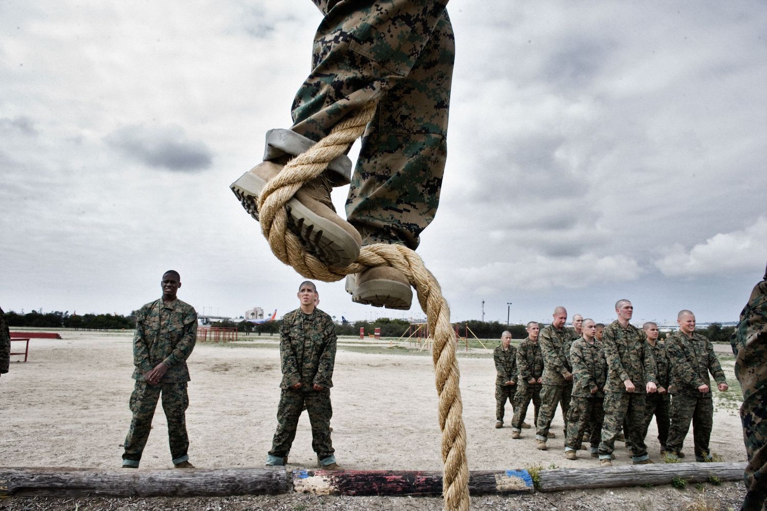 Military training exercises with climbing ropes on a cloudy beach.