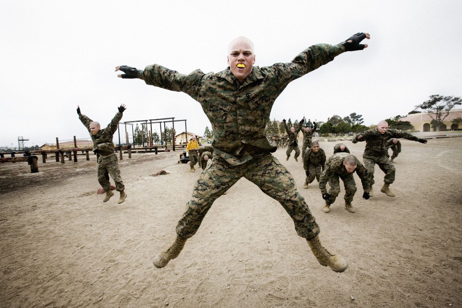 Military personnel executing jumping exercises in combat uniforms on sandy terrain.