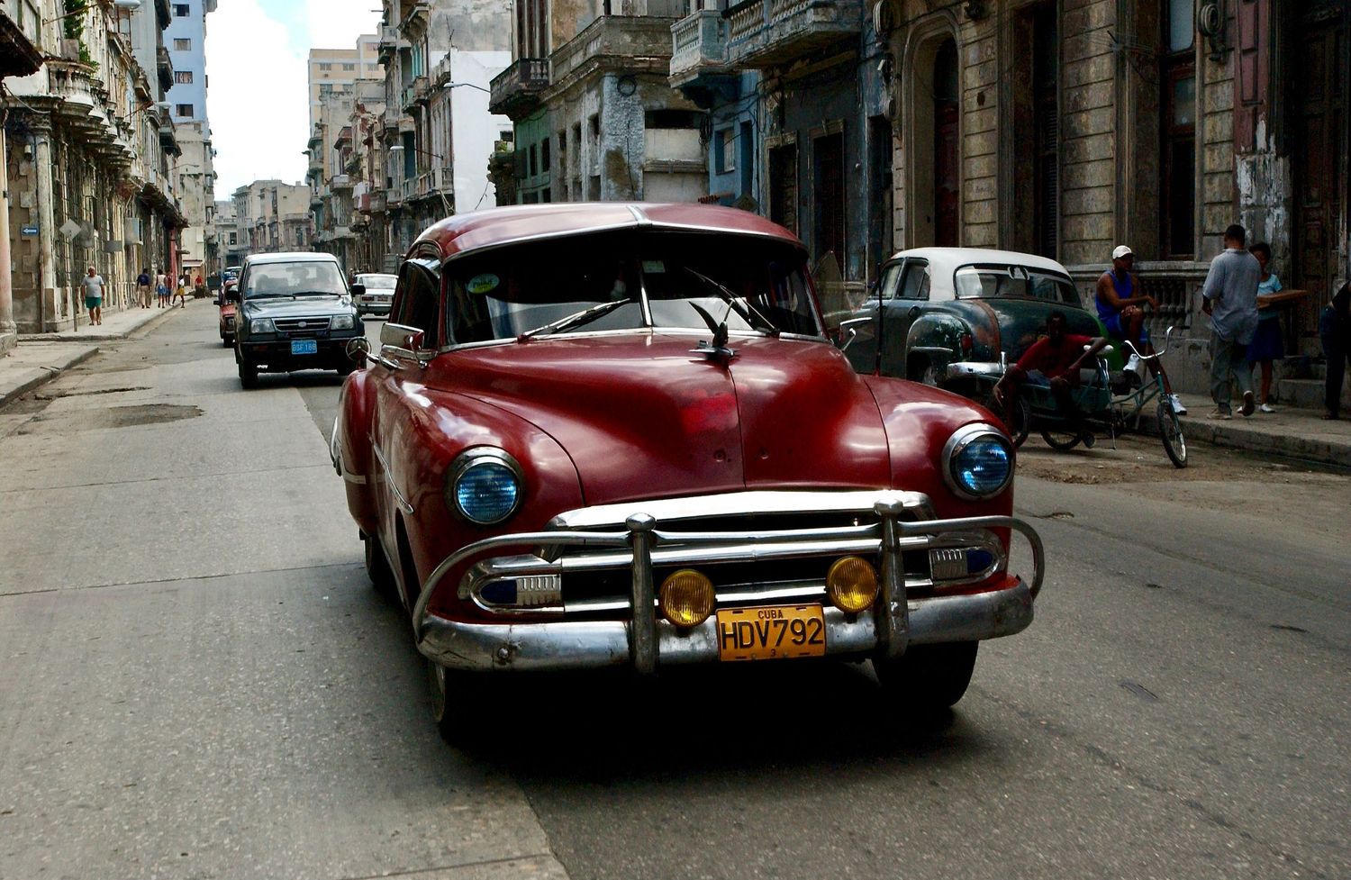 Series of vintage cars parked along streets of Havana with historic architecture in background.