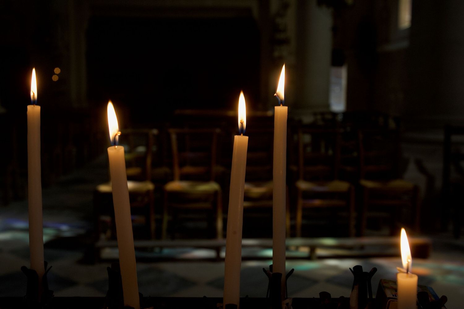 Row of lit candles glowing in a dark church or cathedral setting.