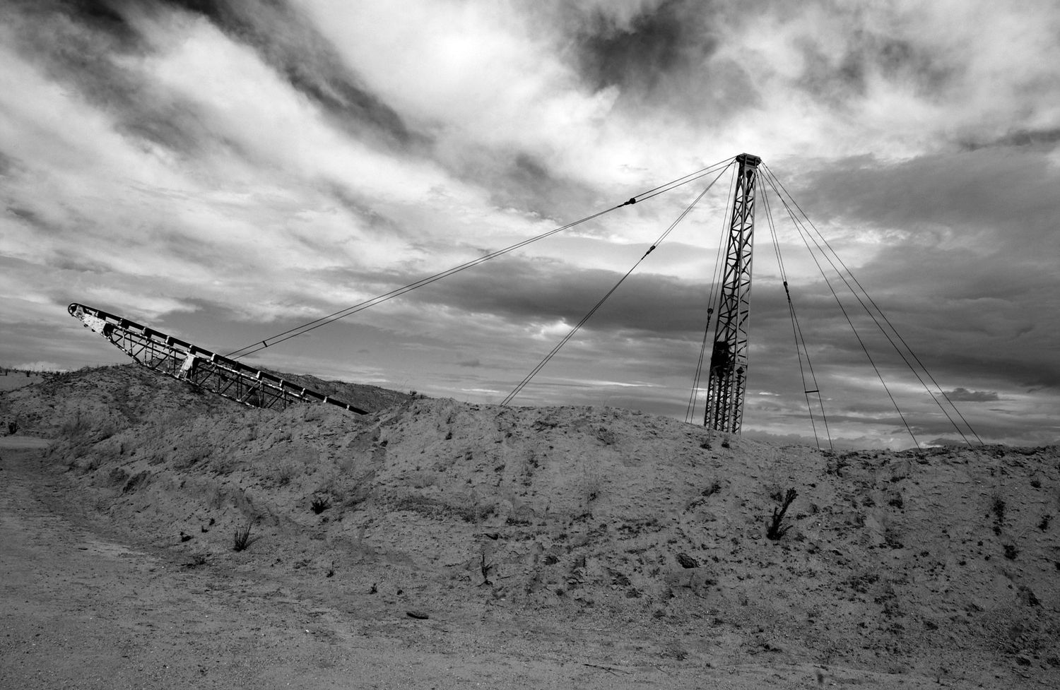Industrial mining equipment and structures silhouetted against cloudy skies in a barren landscape.