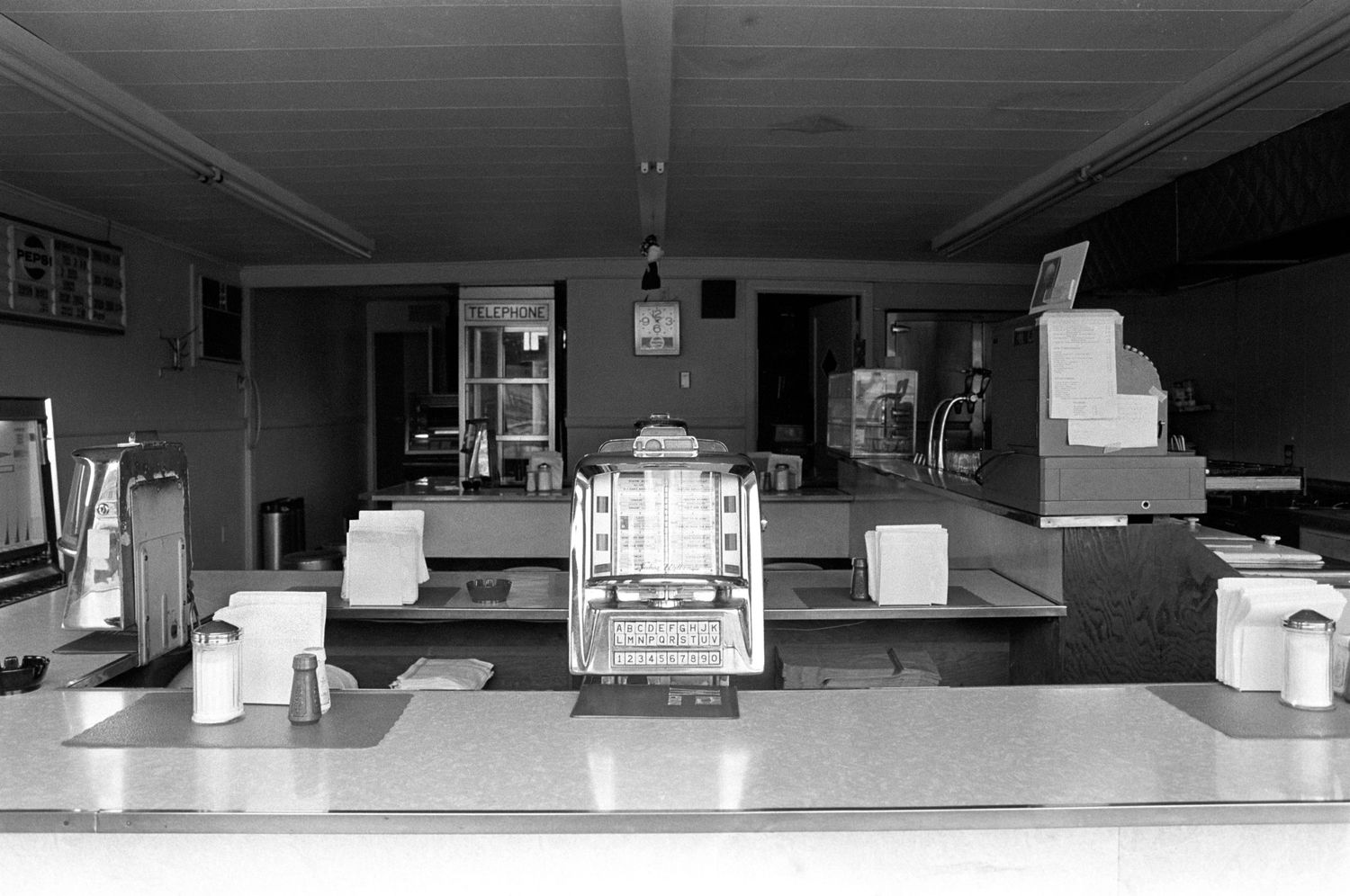 Black and white interior of empty diner counter with bar stools.