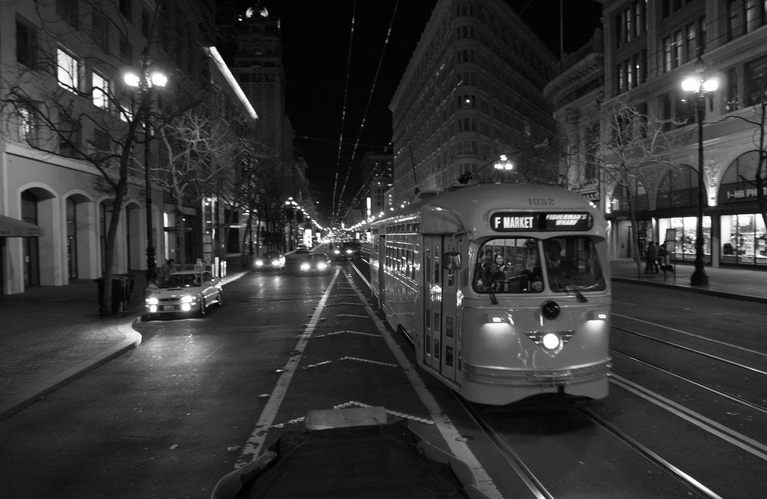 Black and white nighttime street view with illuminated lights reflecting on wet pavement.