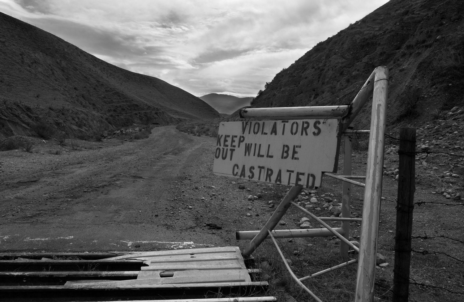 A dramatic black and white landscape of winding mountain roads with power lines stretching into the distance.