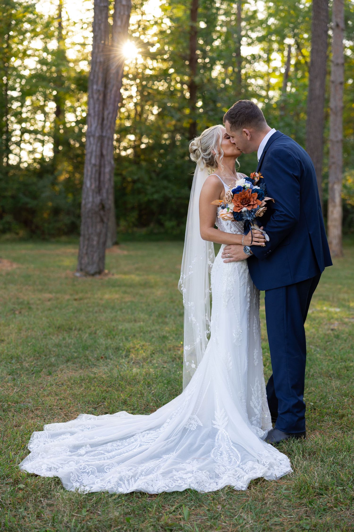 A romantic wedding couple shares intimate moments at sunset in a wooded setting with sunlight filtering through trees.
