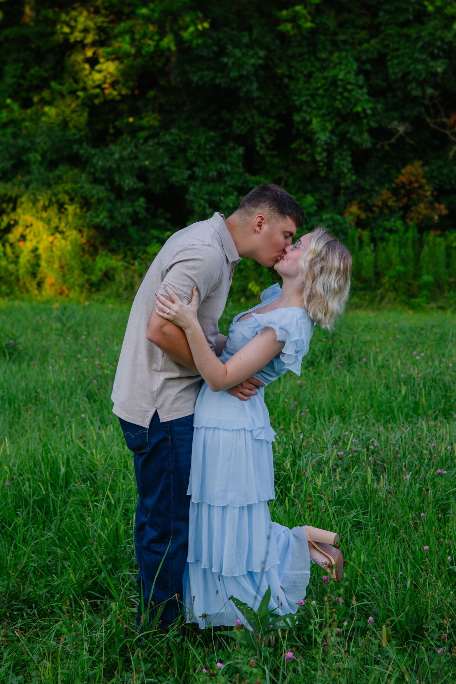 A romantic couple embraces in a lush green field during a summer evening photoshoot.