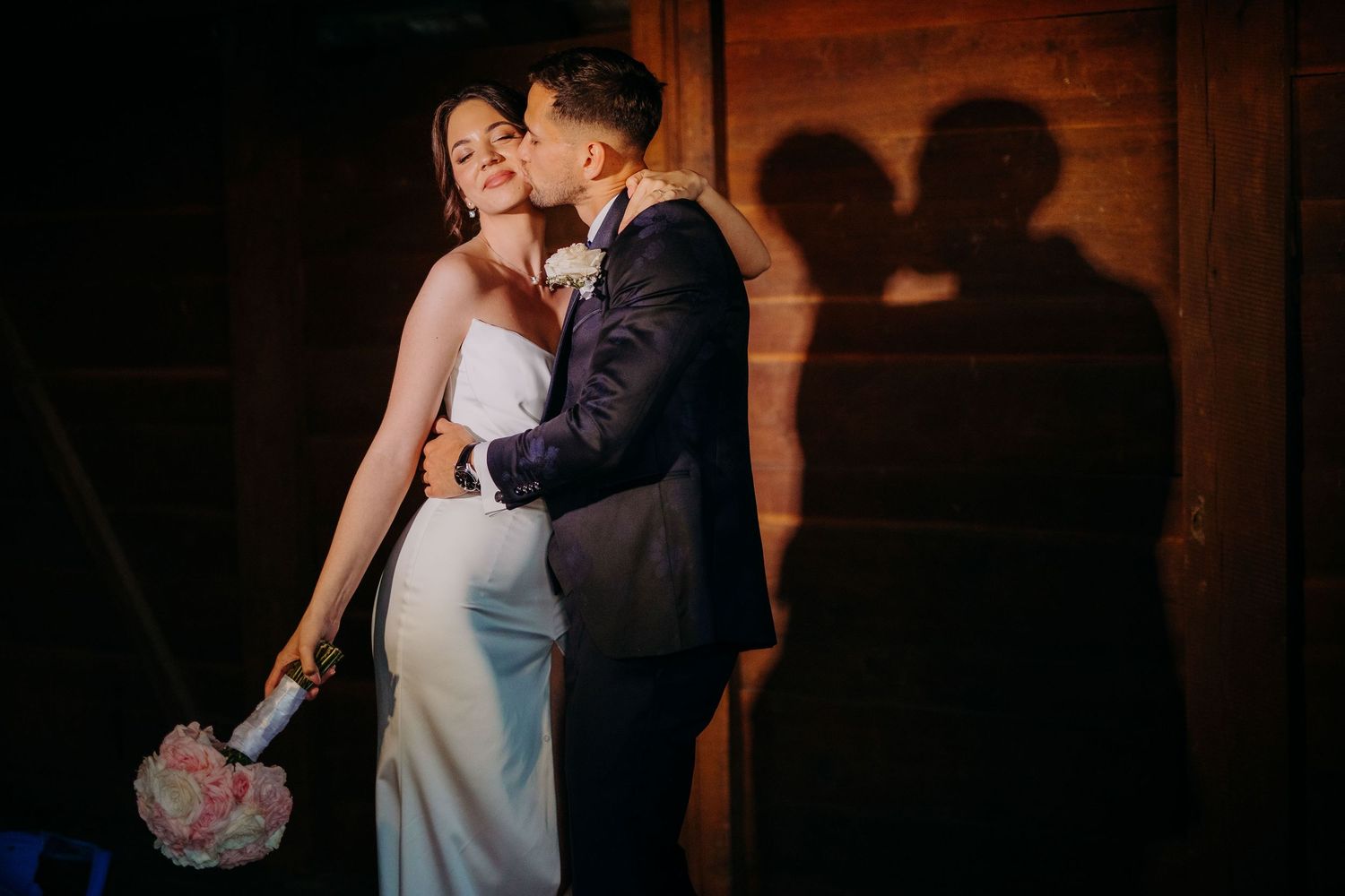 Bride and groom share an intimate moment during sunset kiss at rustic barn wedding.