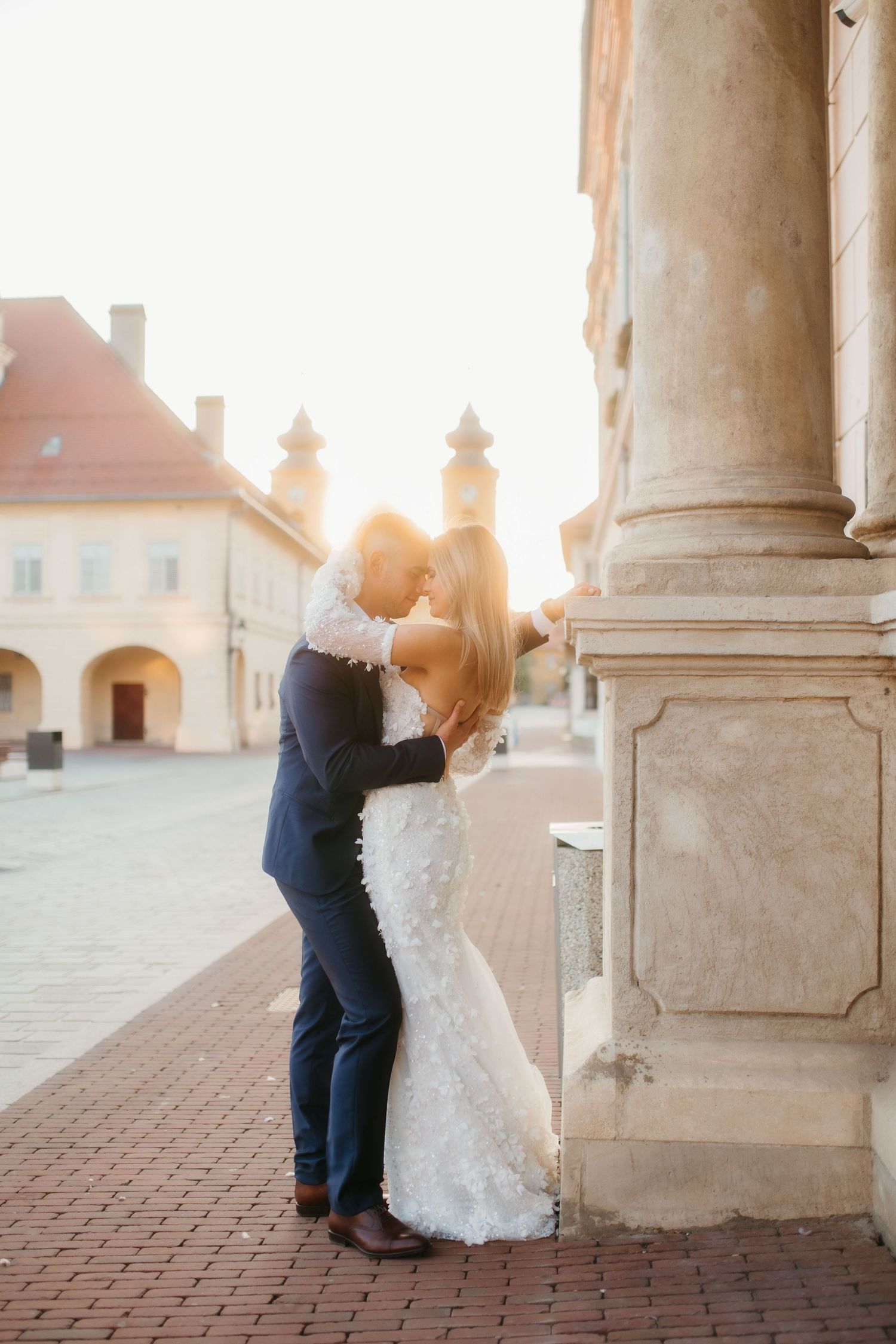A tender moment between newlyweds against historic architecture at sunset.