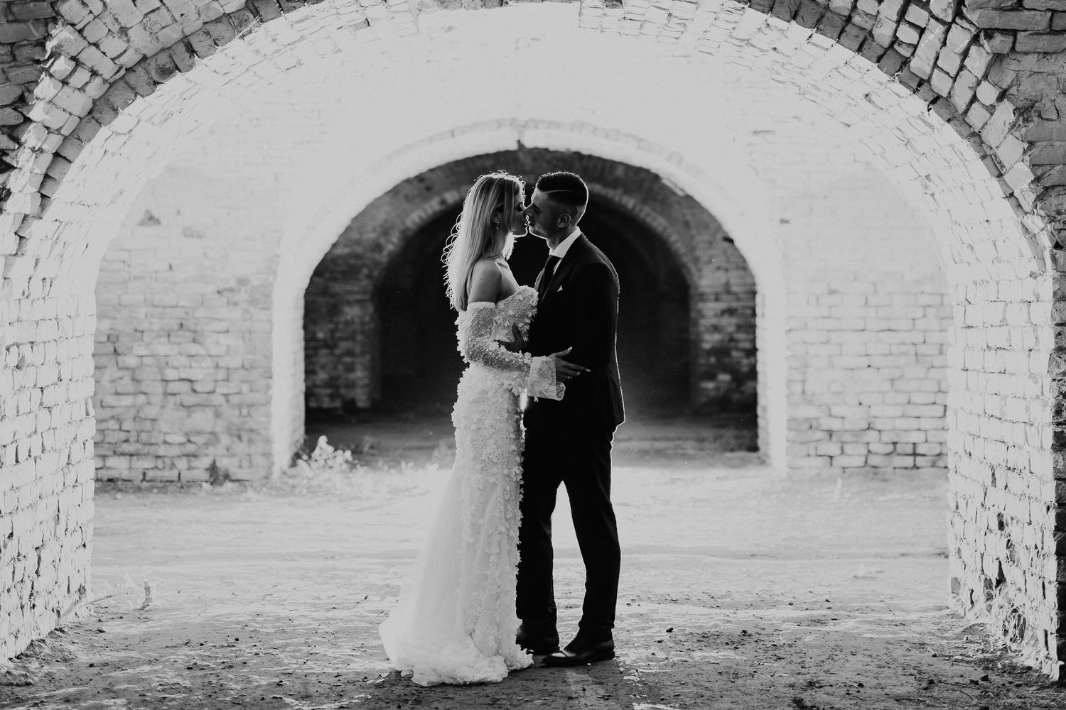 A black and white wedding photo under a vintage brick tunnel archway.