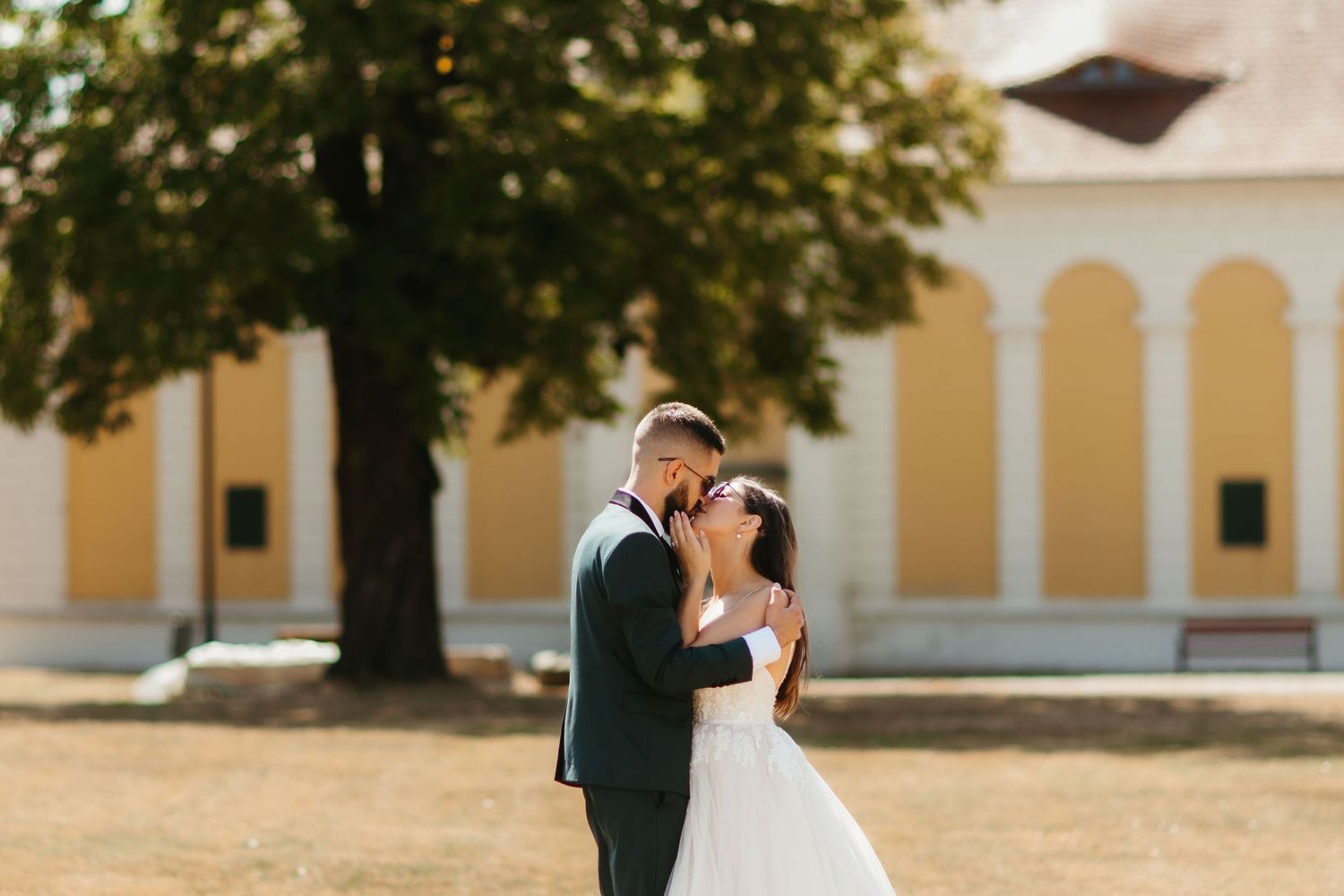 A newlywed couple shares an intimate moment together in front of a yellow building with arched windows.