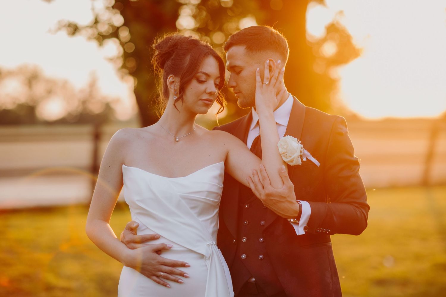 Silhouetted couple embraces in a golden sunset while wearing formal attire in an outdoor setting.