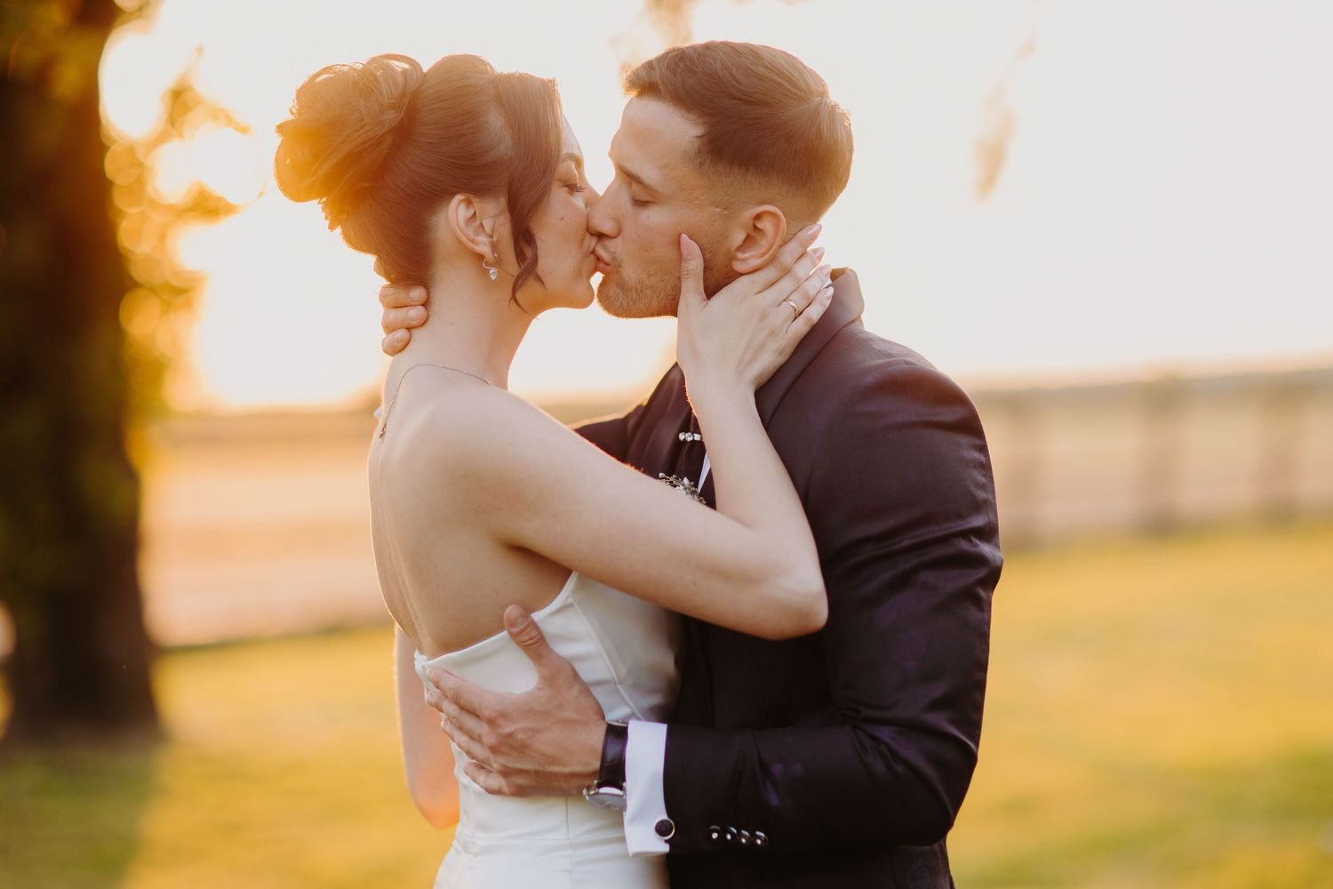 A romantic sunset moment with a couple sharing an intimate embrace in a golden-lit field during golden hour.