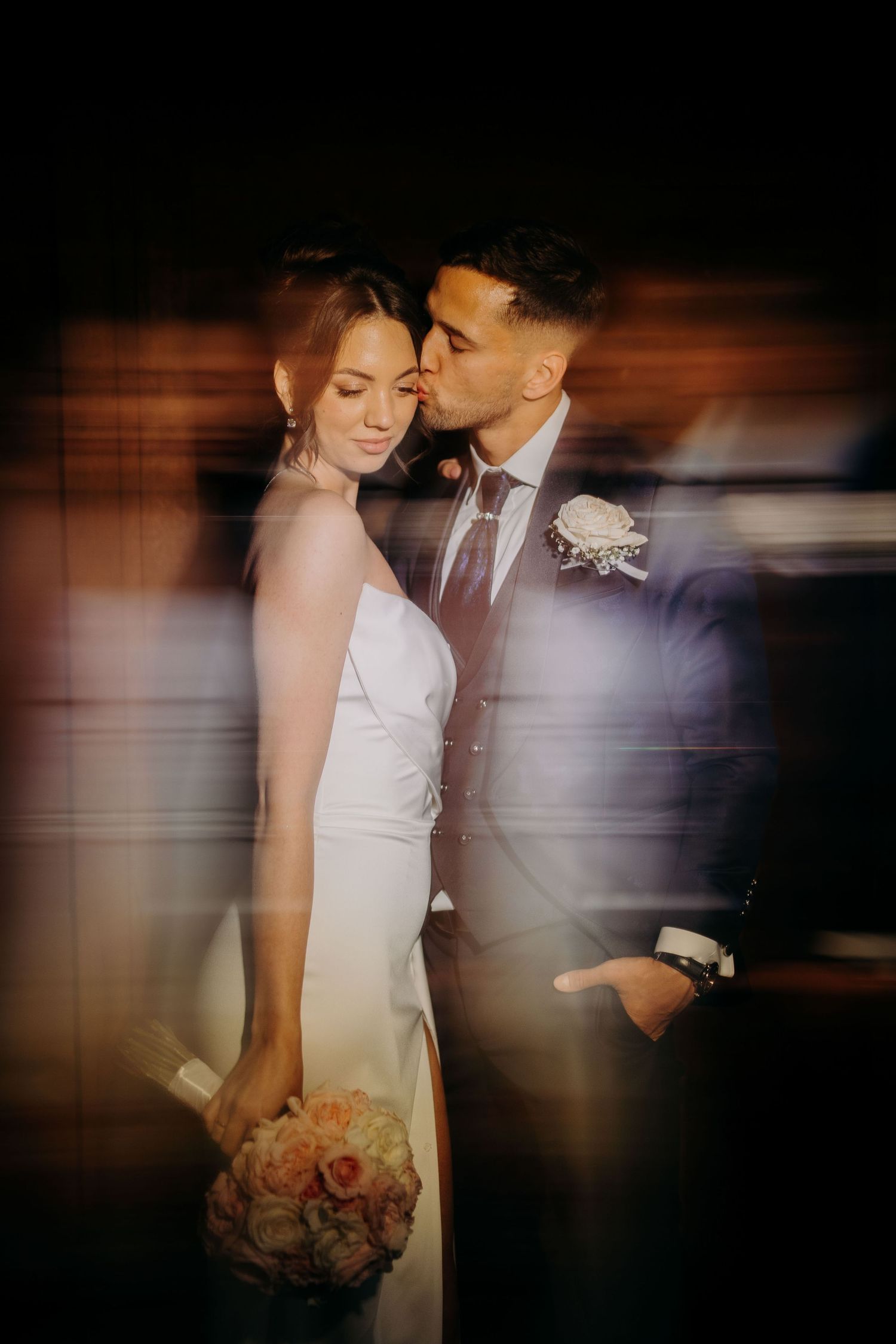 A romantic wedding photo with motion blur effect shows couple embracing while bride holds a peach and pink bouquet.