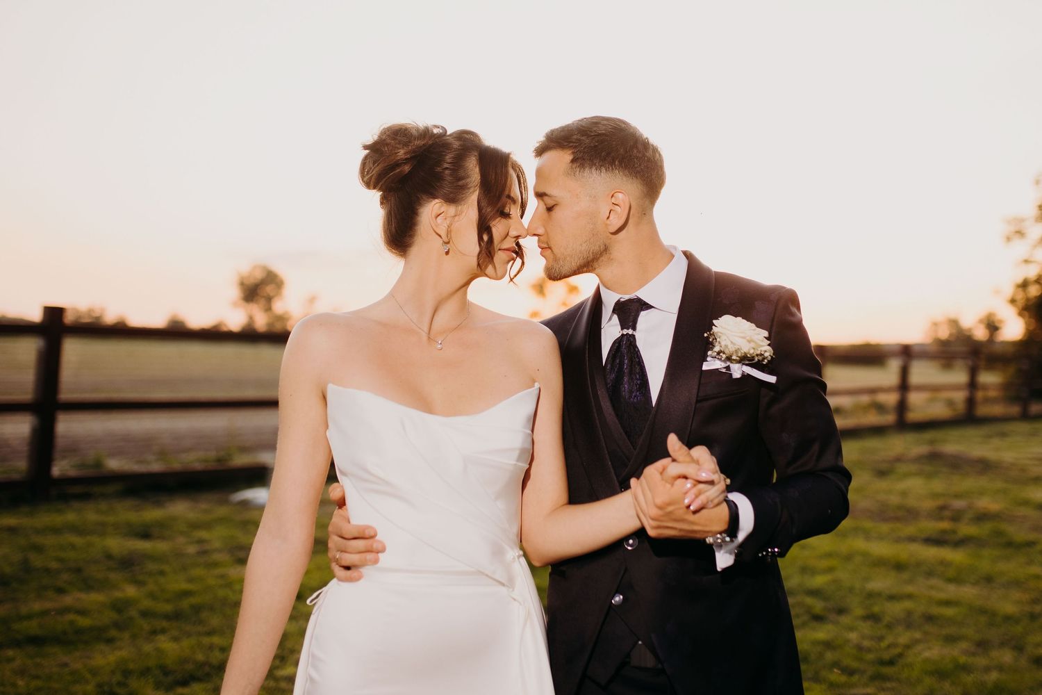 A romantic sunset wedding photo with a couple sharing an intimate moment in front of a rustic fence.